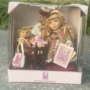 Porcelain doll in box with crib and bear.